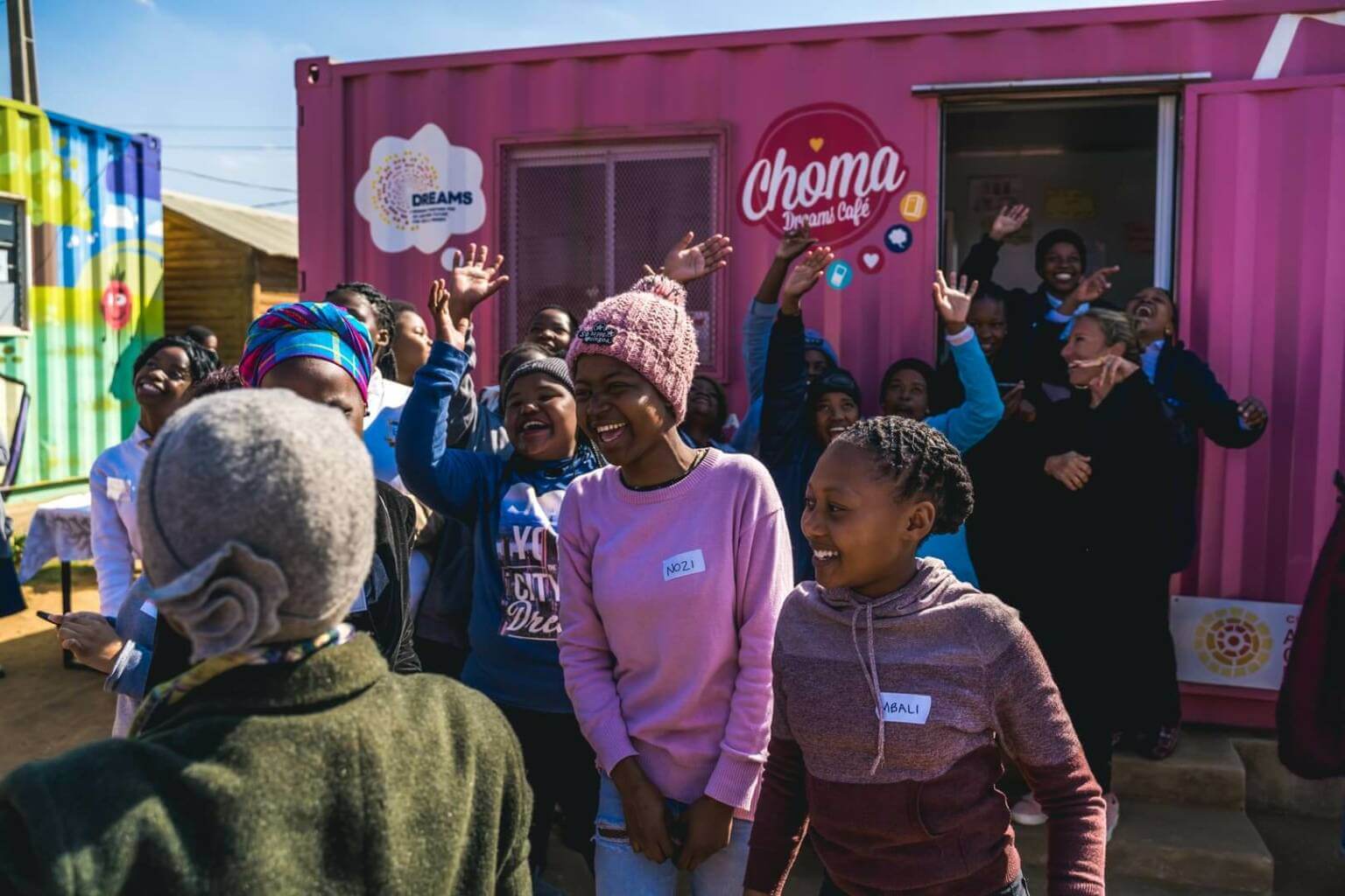 Group of laughing young people in front of a pink Choma Dreams Café trailer