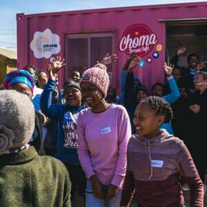 Group of laughing young people in front of a pink Choma Dreams Café trailer