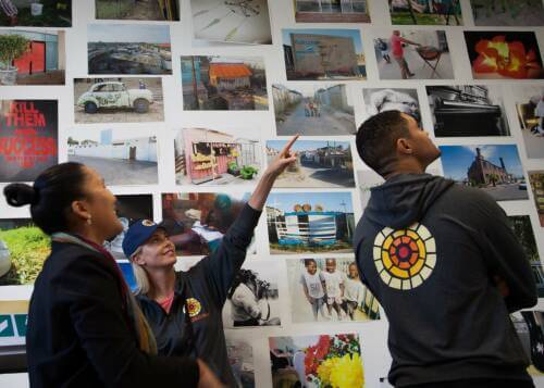 actors Charlize Theron and Trevor Noah looking at a wall of photos from Life Choices