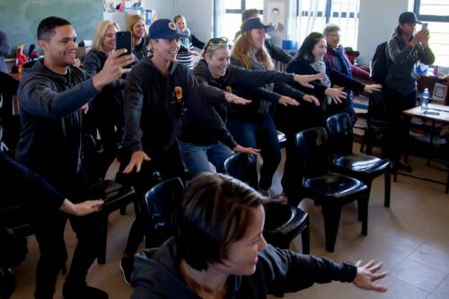 A group of people including actors Charlize Theron and Trevor Noah doing a classroom exercise