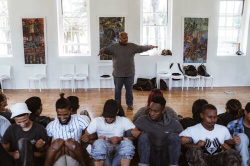 A man at the front of a classroom leading young people in a group exercise